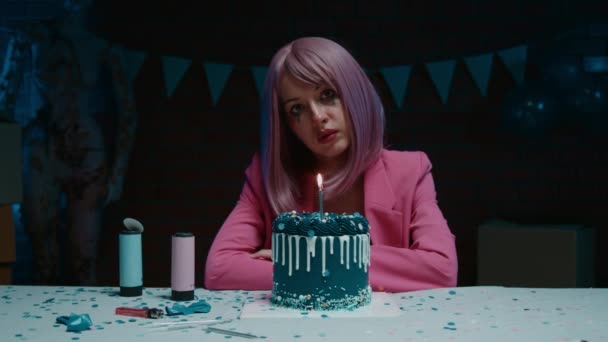 悲伤的粉红头发的生日女孩 化着妆 泪汪汪的眼睛 穿着粉红的运动衫 坐在桌旁 在一间装饰着生日装饰品的黑暗的房间里 享用着蓝色的生日蛋糕 高质量的4K镜头 — 图库视频影像
