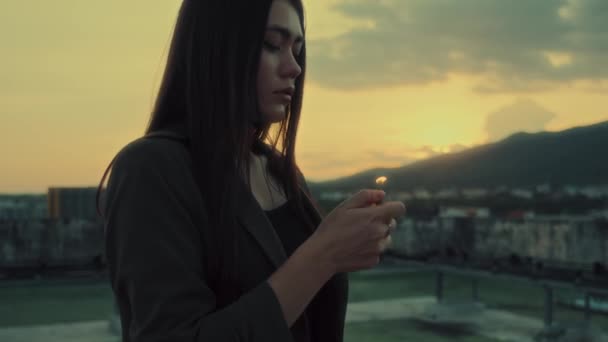 在美丽的落日下 一位年轻的亚洲女孩在屋顶上点燃打火机的特写 她的照片上有山景 遥望远方 青春的概念4K镜头 高质量的4K镜头 — 图库视频影像