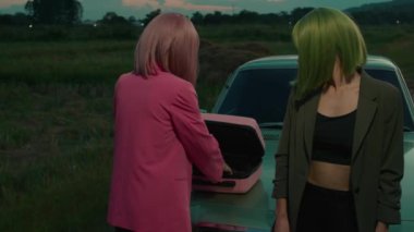 Pembe saçlı kız ve yeşil boyalı saçlı kız arkadaşı, arabanın yanındaki gözlükleriyle sigaralarını çıkartıyorlar. 4K 'lık kaliteli görüntü. Yavaş çekim