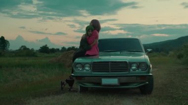 Yeşil saçlı kız, pembe saçlı kız arkadaşına sıkıca sarılıyor. Dışarıdaki eski arabanın üstünde dağ manzaralı. Yüksek kalite 4K görüntü. Yavaş çekim, sinematik.