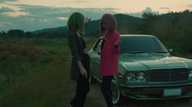 Yeşil ve pembe kısa saçlı bir çift açık havada, eski arabanın yanında dans ediyor. Yüksek kalite 4K görüntü. Yavaş çekim, sinematik.