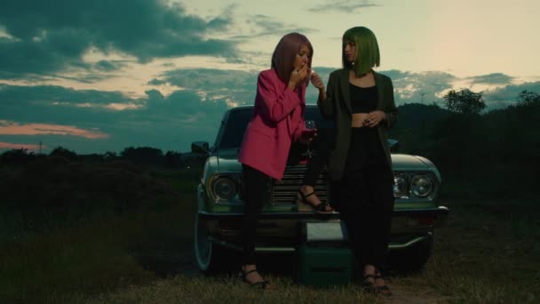 在户外有山景的复古汽车前 一对粉红和绿色波布头发的女情侣点着一支香烟 慢动作 — 图库视频影像