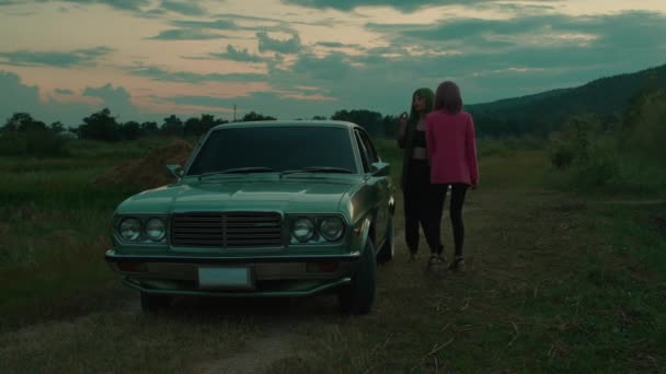 緑とピンクのボブヘアカットのガールカップルは 山の景色と屋外のレトロカーの近くでダンスや喫煙 高品質の4K映像 スローモーション — ストック動画