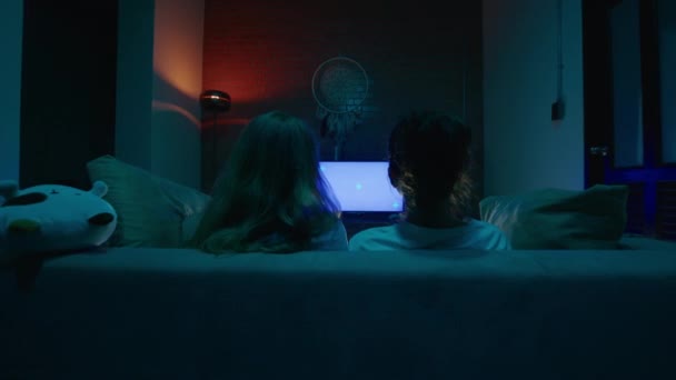 从两个年轻女人的后面放大 坐在舒适的沙发上拥抱 晚上看电影 滑行射击 蓝色的黑暗客厅 高质量的4K镜头 — 图库视频影像