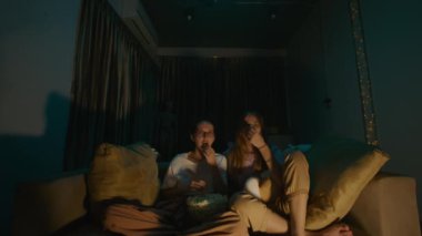 Evdeki rahat bir kanepede oturup pijamalarıyla patlamış mısır yiyen iki genç kadın gece televizyon izlerken. Karanlık odada TV ışığı ve gölgeler. Yüz ifadesi. Yüksek kalite 4k görüntü