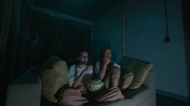 两名年轻妇女穿着睡衣坐在舒适的沙发上吃爆米花 晚上看电视 高质量的4K镜头 — 图库视频影像