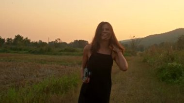 Genç, gülümseyen bir esmer, eski bir kamerayla bir yaz günü gün batımında etrafta dönüyor ve zıplıyor. Boş zaman aktiviteleri, seyahat, hobi. Yüksek kalite 4k görüntü