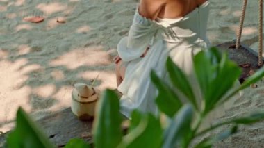 Beyaz elbiseli bir kadın sahilde salıncakta sallanıyor. Etrafı karasal bitkiler ve otlarla çevrili. Huzurlu manzaranın tadını çıkarırken çıplak ayağı hafifçe yere değiyor.