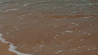 Kumlu kıyı şeridine çarpan bir dalganın yakın çekimi sahilin zeminiyle suyun buluştuğu güzel bir manzara yaratır.