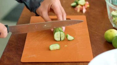 Bir el, ahşap bir kesme tahtasındaki salatalığı dilimliyor. Yemek malzemesi sofra takımı ve kesim tahtası kullanarak yemek tarifi için hazırlanıyor.