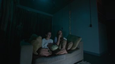Evdeki rahat bir kanepede oturup pijamalarıyla patlamış mısır yiyen iki genç kadın gece televizyon izlerken. Yüksek kalite 4k görüntü