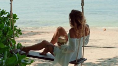 Bir kadın sahildeki hindistan cevizi ağacında sallanıyor, göl kenarında boş vakitlerin tadını çıkarıyor. Manzara sakin ve eğlenceli bir plaj olayı için mükemmel.
