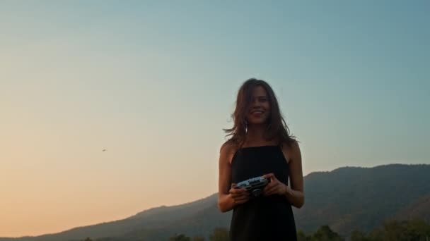 若い笑顔の女性は 夏の日に山の背景を持つフィールドの古いカメラで写真を撮ります レトロカメラ レジャー活動 高品質の4K映像 — ストック動画