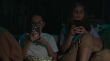 Evdeki rahat bir kanepede oturup geceleri televizyon izlerken telefonlarında oturup pijamalarıyla patlamış mısır yiyen iki genç kadının portresi. Karanlık odada televizyon ışığı. Akıllı telefonlar dikkatimi dağıttı. Yüksek