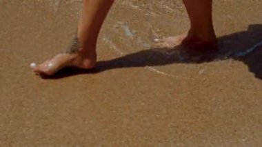 Kişi ayakları kumsaldaki ıslak toprağa batıyor, etrafı ağaç gövdesine benzeyen sert ahşap döşemelerle çevrili.