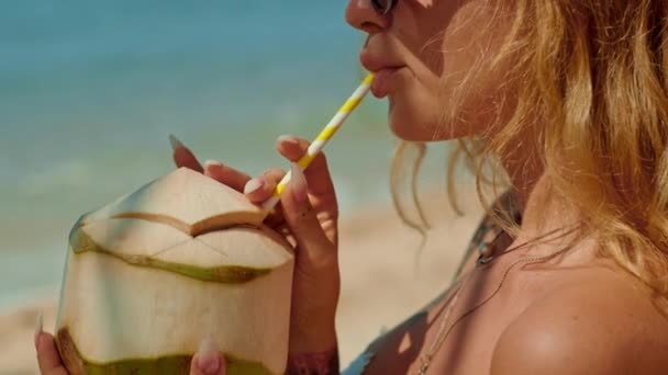 サーファーヘアの女性は ビーチのわらを通って喜んでココナッツ水を飲み 水で彼女のゆったりとした時間を楽しんでいます — ストック動画