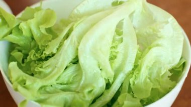 Bir tabak yaprak sebze, ahşap bir masada marul yapraklarıyla dolu beyaz bir kase, lezzetli bir bitki tabanlı yemek için taze bir malzeme.