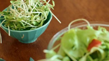 Salatanın yanında canlı filizler ve ahşap bir masada cam bir kasede hazırlanan salata malzemelerinin yakın plan çekimi. Sağlıklı gıda hazırlığının özünü doğal malzemelerle yakalamak.