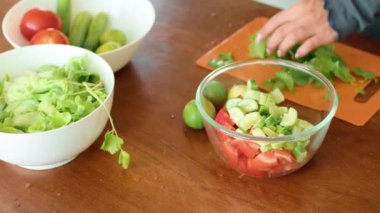 Tabaklar dolusu yeşil sebze ve taze salata ile dolu ahşap bir masa. Sağlıklı ve lezzetli bir yemek tarifi için çeşitli malzemeler sergileniyor.