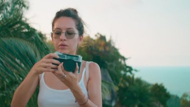 Gözlüklü bir kadın klasik bir film kamerasıyla okyanusu ve gökyüzünü çekiyor.