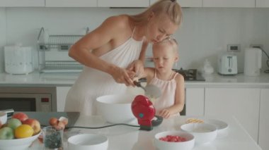 Anne ve kızı beyaz bir mutfakta birlikte waffle yapıyorlar.