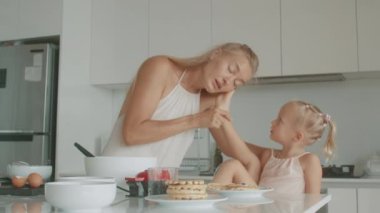 Bir anne, yemek takımları ve bulaşık takımlarıyla çevrili olarak mutfakta bebeğini sevgiyle öper. Mutlular ve birlikte yemek hazırlıyorlar.