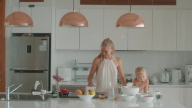 Sevgi dolu anne ve küçük kızın hamur işi pişirirken eğlenmesi, şeker tozu serpmesi, gülmesi, mutlu olması, sıcak mutfakta aylak aylak dolaşması. Aile eğlencesi. Yüksek kalite 4k