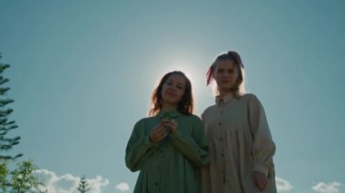 Güneşli bir günde dışarıda poz veren neşeli genç kadınlar kameraya bakıp gülümsüyorlar. Kırsalda bir çimenlikte duran iki kız arkadaş. Yüksek kalite 4k görüntü
