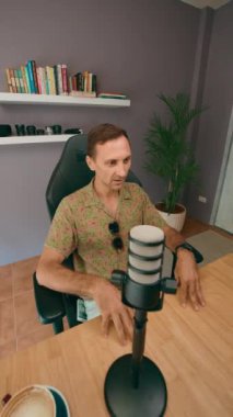 Bir adam şık stüdyosunda birinci sınıf mikrofon ve kamera ekipmanıyla podcast içeriği yaratıyor.