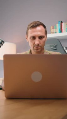 Kitap rafı ve lambasıyla modern bir ofis ortamında dizüstü bilgisayarda çalışan odaklanmış bir adam..