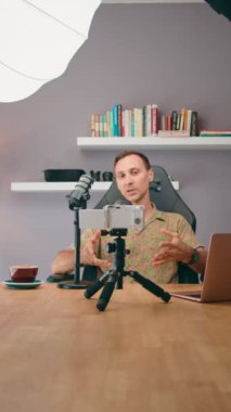 İçerik yaratan bir adam, evinde mikrofon, akıllı telefon ve tripod kurulumu kullanarak bir podcast kaydediyor.