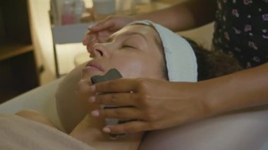 Yüz masajı için gua sha aracıyla sakin bir spa sahnesi. Cilt bakımını ve rahatlığını teşvik ediyor.