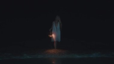 Beyaz elbiseli gizemli bir kadın gece elinde fenerle denize dalıyor ve ürkütücü bir atmosfer yaratıyor..
