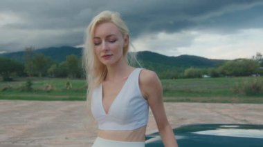 Beyaz elbiseli bir kadın, yeşil bir arabanın yanında kırsal alanda özgürlüğün ve zarafetin simgesi.