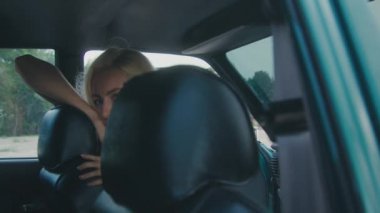 Beyaz elbiseli bir kadın kırsalda klasik bir arabada oturuyor, özgürlüğü ve zarafeti simgeliyor.