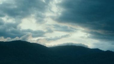 Tepelerin üstündeki mavi gökyüzünde hareket eden kara bulutların zamanı. Bulutların şekil değiştirdiği, zaman atlamalı doğa arkaplanı. Hava değişikliği. Doğa, gökyüzü bulutları, tepeler. Yüksek kalite 4k görüntü