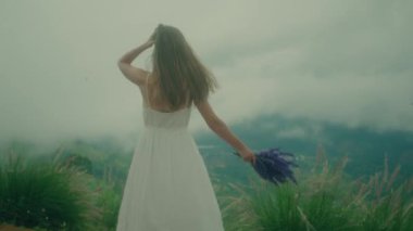 Beyaz elbiseli bir kadın bulutlu bir gökyüzünün altında neşeyle dans eder, mutluluk ve özgürlük saçar.