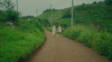 Beyaz elbiseli iki kadın neşe içinde güzel, yemyeşil bir yolda koşar, birlikte doğadan zevk alırlar.