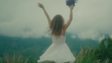 Beyaz elbiseli bir kadın bulutlu bir gökyüzünün altında neşeyle dans eder, mutluluk ve özgürlük saçar.