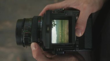 Eski bir kamerayı tutan ve doğanın güzelliğini objektiften gösteren ellerin yakın çekim görüntüsü..