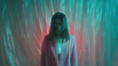Yavaş deklanşör efekti, pembe ceketli genç bir kadın neon ışıklı plastik filmin arka planına doğru hareket ediyor.
