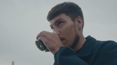 Genç bir adam nefes kesici ve canlı bir açık hava ortamında dikilirken rengarenk bir kutudan rastgele yudumluyor.