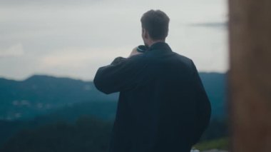 Genç bir adam nefes kesici ve canlı bir açık hava ortamında dikilirken rengarenk bir kutudan rastgele yudumluyor.