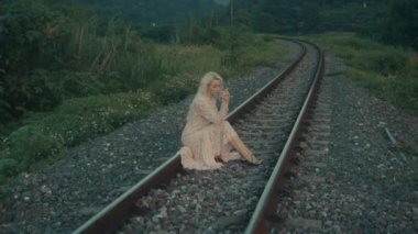 Evrak çantalı klasik bir kadın, sakin ve sakin kırsal bir manzarayla çevrili demiryolu raylarında tek başına oturur..