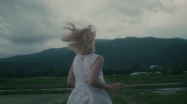 Kamera, dağa doğru korkuyla koşan beyaz elbiseli genç bir kadını takip ediyor. el kamerası görüntüsü