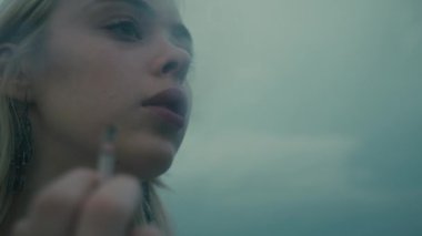 Genç bir kadın puslu bir ortamda sigara içiyor, bir anlık içgözlem ve keşif anı yakalıyor.