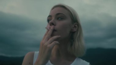 Genç bir kadın puslu bir ortamda sigara içiyor, bir anlık içgözlem ve keşif anı yakalıyor.