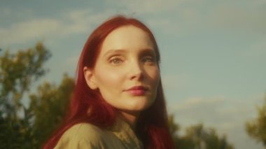 Mandalina tarlasında güzel bir gün batımında elinde sepetle parlak, yemyeşil bir sepetle gezen kızıl bir kadının görüntüsü.