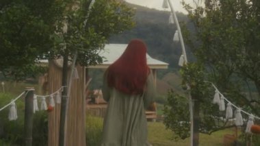 Kızıl saçlı kız gün batımında turuncu dağlarda bahçede yürüyor. 