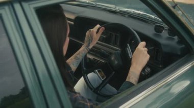 Kadın, köy yolunda bozulan eski bir arabayı çalıştırmaya çalışıyor. 